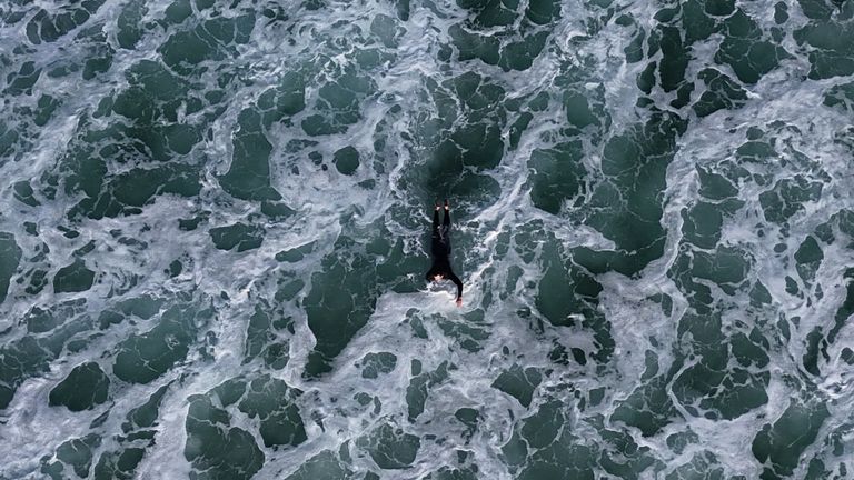 A surfer paddling through dark turquoise water