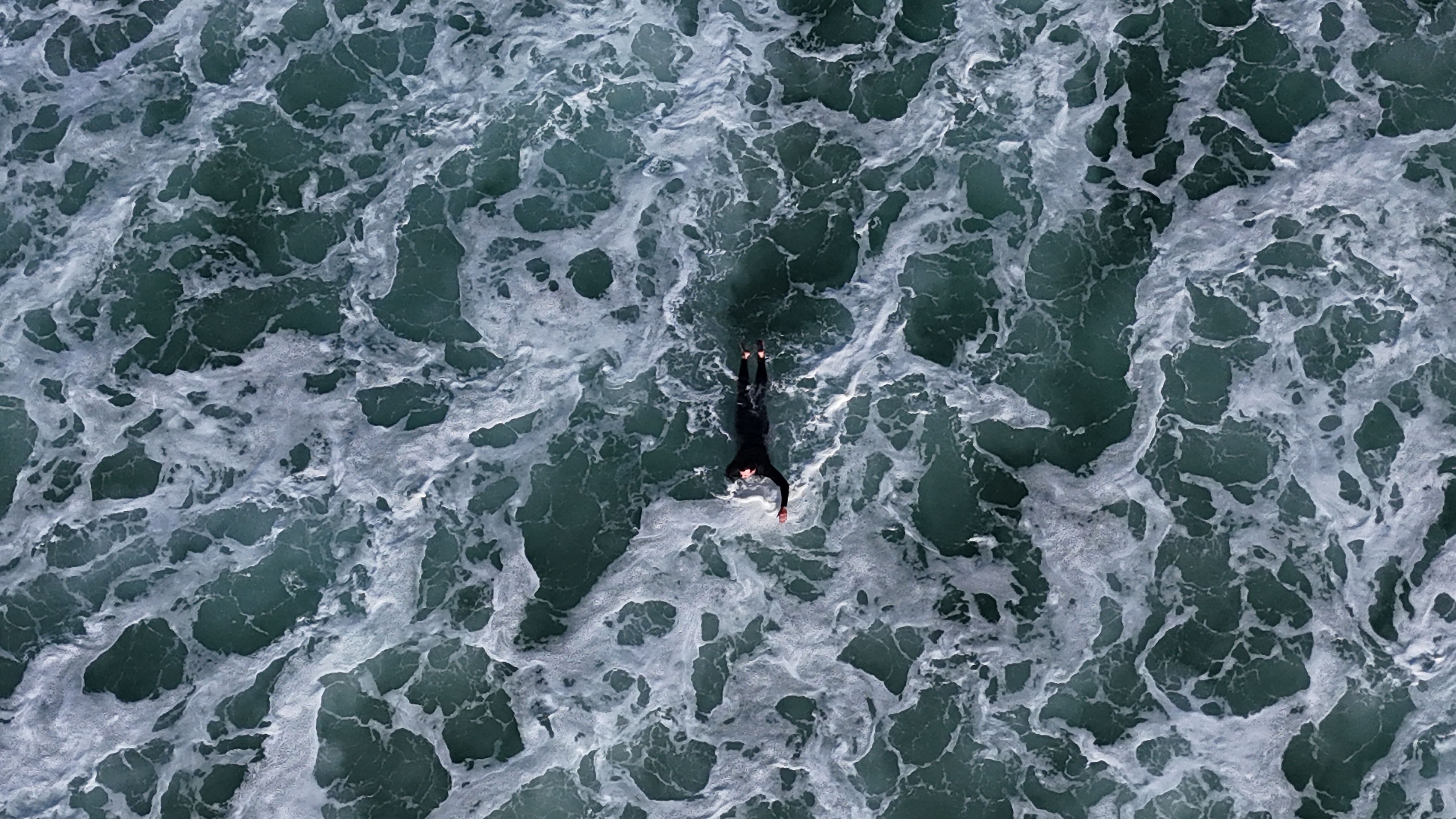 A surfer paddling through dark turquoise water