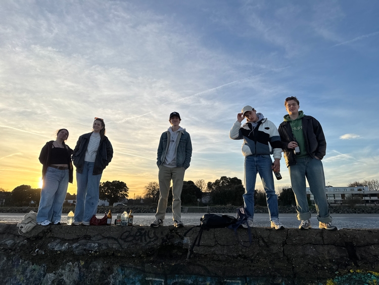 Ioli, Kadin, Tom, Mo, and Max standing on a wall at the beach