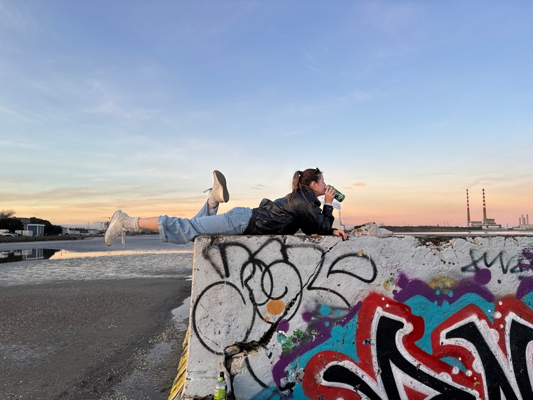 Kadin posing on a wall at the beach drinking a beer