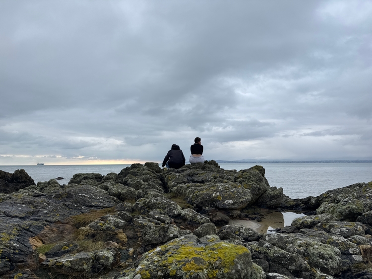 Ioli and Kadin sitting on some rocks looking out to the sea