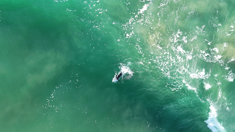 A surfer paddling through light turquoise water